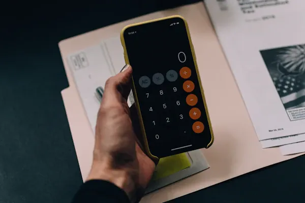 Calculator app on a phone held over a folder of tax papers